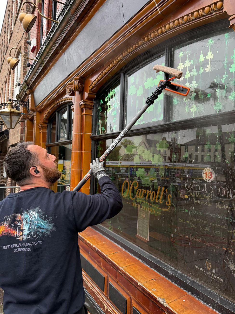 Liam cleaning the front windows of O'Carroll's bar with a pole-mounted squeegee.