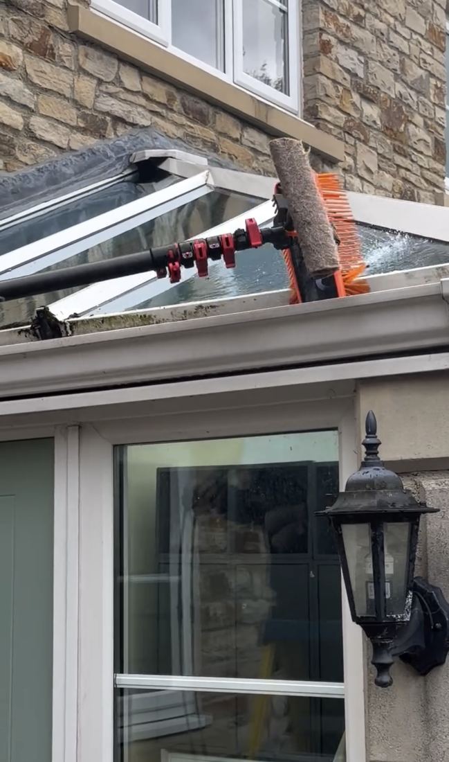 A brush working close up across the glazing bars of a lantern-style conservatory roof.