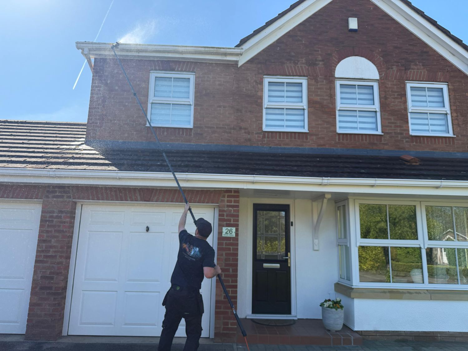 Fascia and soffit being washed down from the ground with an extending pole on a detached house.