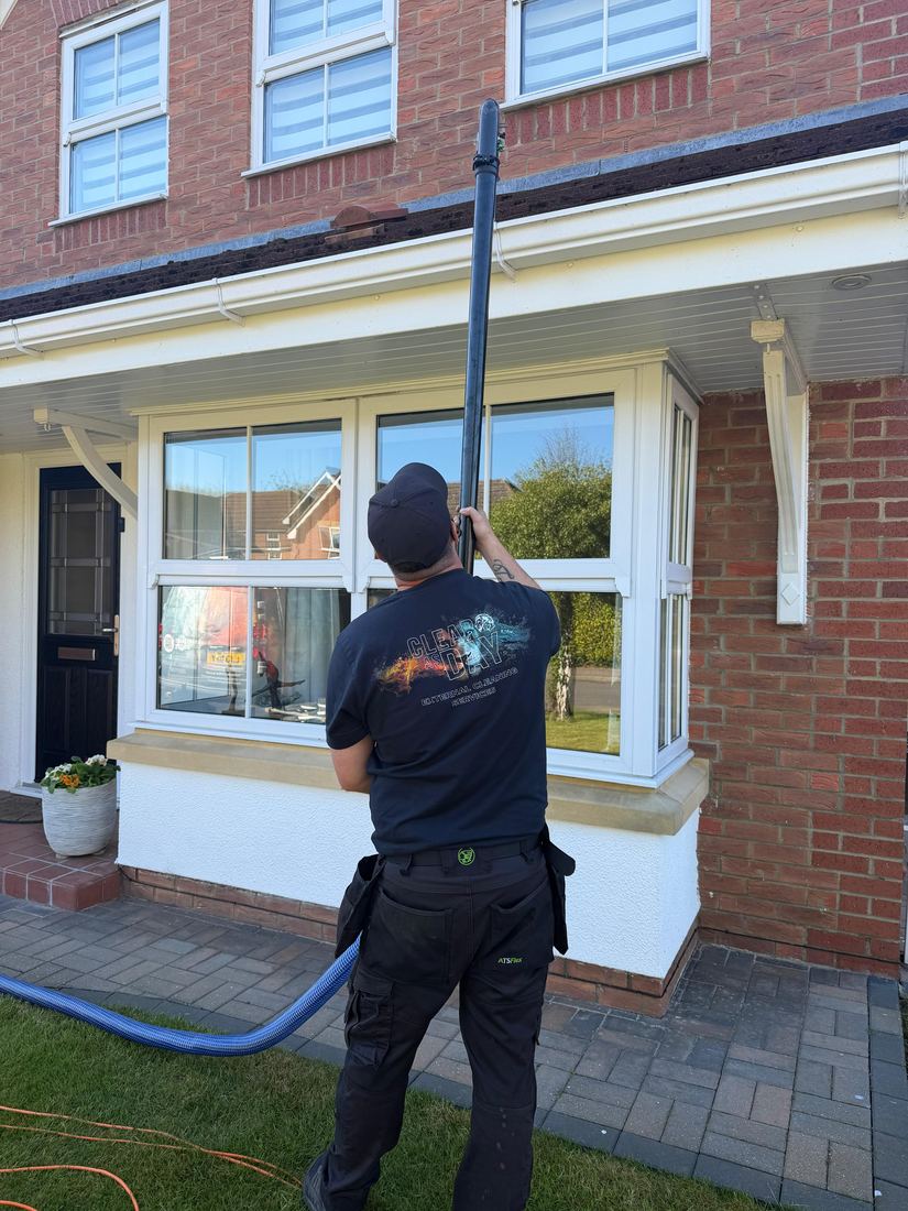 The high-reach vacuum hose run up to the gutter line above a bay window.