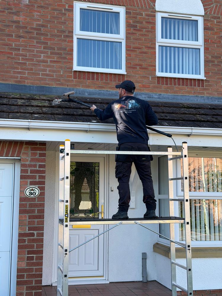 Working from a trestle along a single-storey roof, scraping it clear.