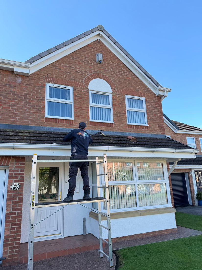 Working from a trestle along the roof of a single-storey extension, scraping it clear.